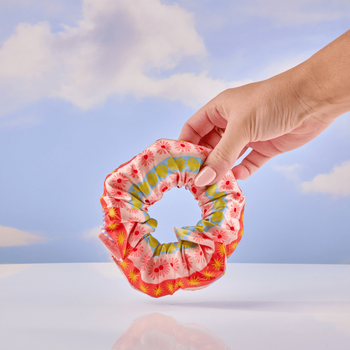 Hand holding a colorful scrunchie against a blue sky background