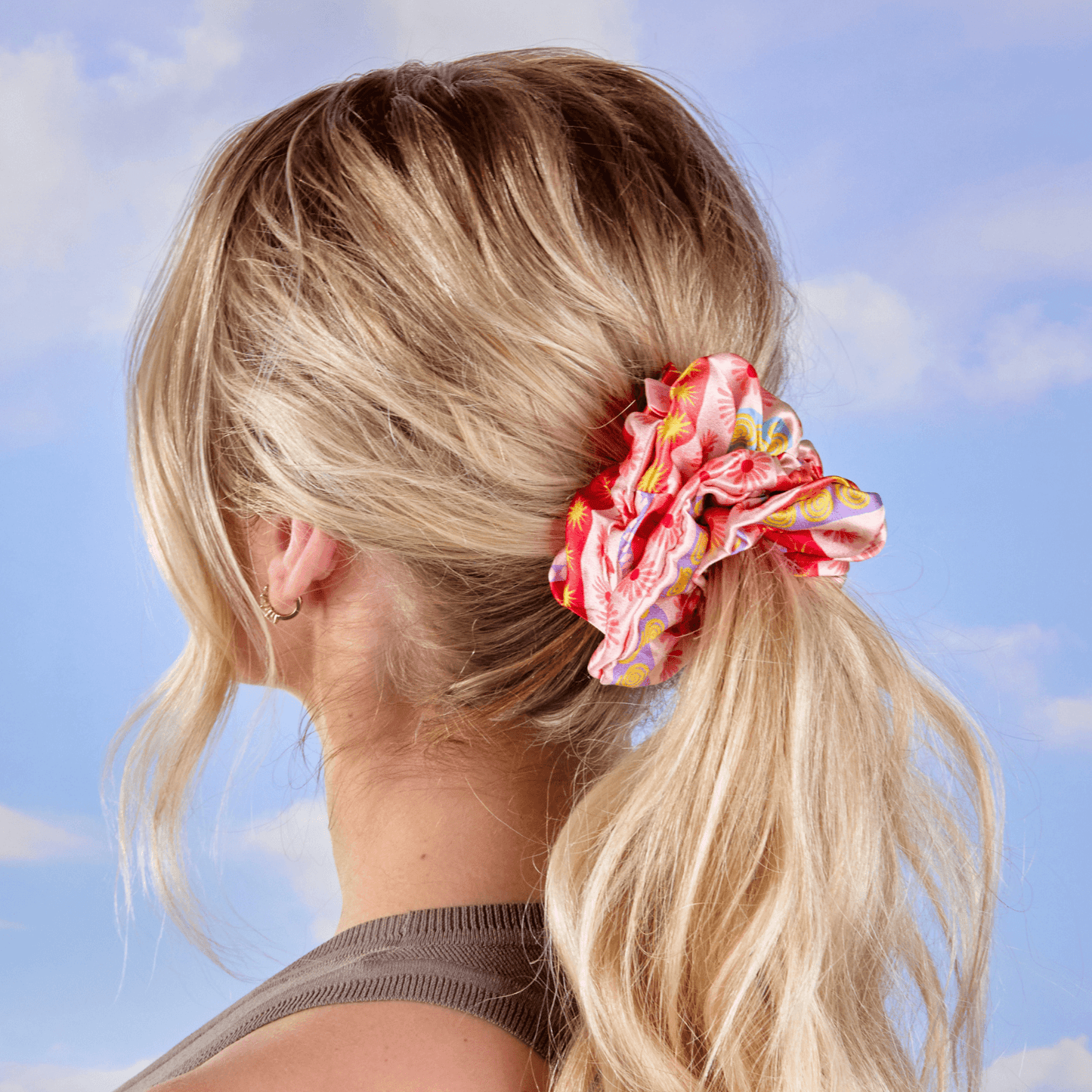 Woman with blonde hair tied in a ponytail with a colorful scrunchie against a blue sky background