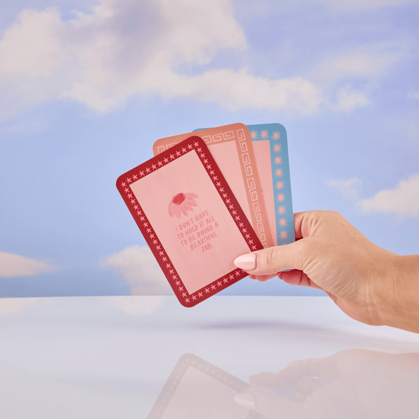 Hand holding three affirmation cards against a sky background