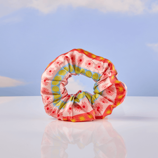 Colorful patterned scrunchie on a reflective surface with a blue sky background